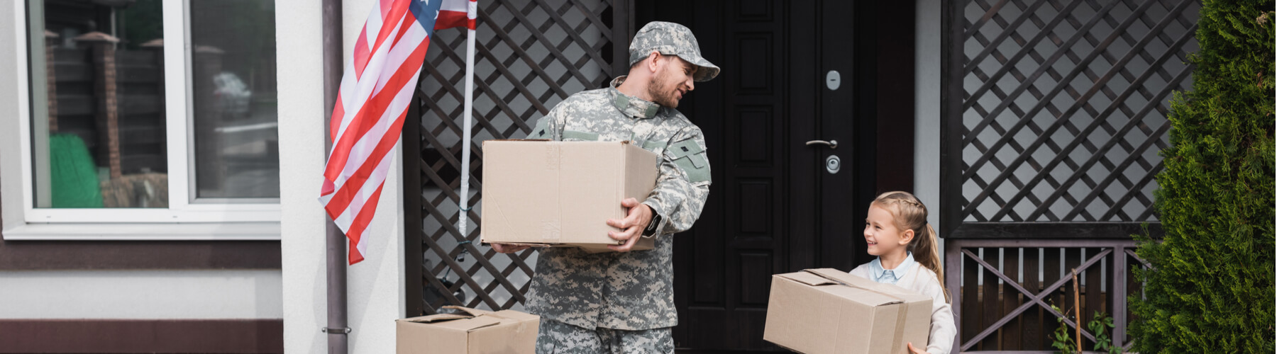 Father in military uniform and daughter holding cardboard boxes near house with american flag, moving in or out of military house
