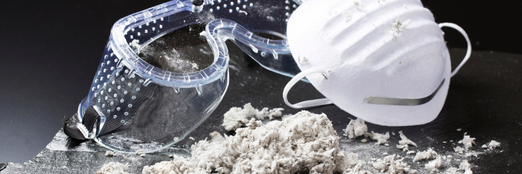 Safety equipment including protective goggles and respirator mask sit beside a pile of fibrous asbestos material, highlighting the critical importance of proper protection when handling this carcinogenic substance