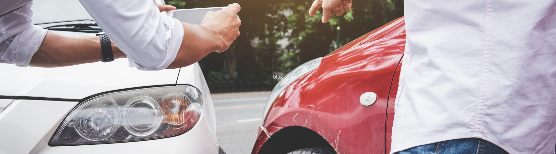 Two people documenting a car accident, with one person taking photos of damage between a white and red vehicle that have collided