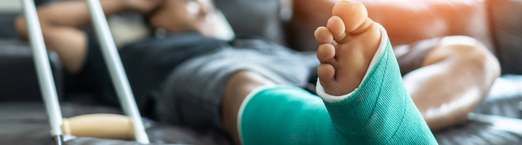 man laying on a couch with a broken foot or ankle, cast on lower leg with crutch propped against couch, commercial injury or premises liability concept