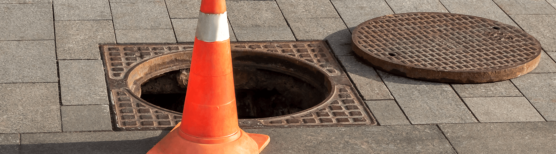 Open manhole cover with a traffic cone in front of it