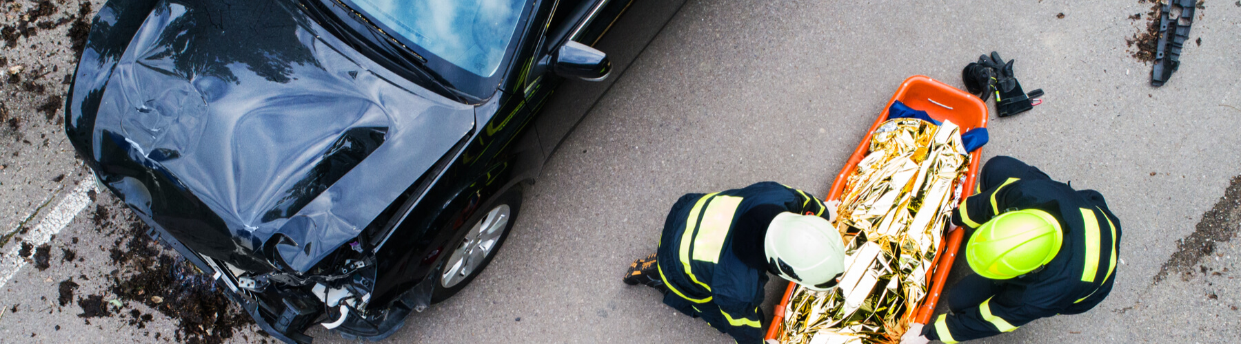 An injured woman in a plastic stretcher after a car accident, covered by thermal blanket.