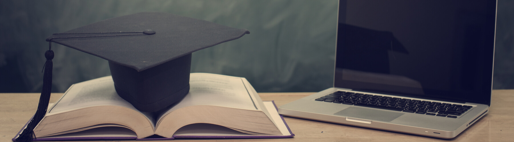 work study concept, open text book with graduate cap on top, sitting next to laptop