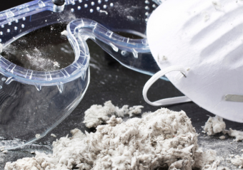 Safety equipment including protective goggles and respirator mask sit beside a pile of fibrous asbestos material, highlighting the critical importance of proper protection when handling this carcinogenic substance