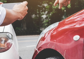 Two people documenting a car accident, with one person taking photos of damage between a white and red vehicle that have collided