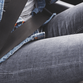 close up image of young adult female wearing jeans buckling her seatbelt in car