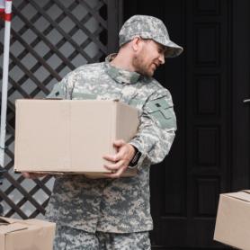 Father in military uniform and daughter holding cardboard boxes near house with american flag, moving in or out of military house