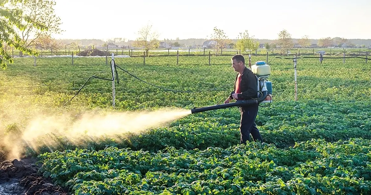 Farmer spraying pesticides in a crop field, representing toxic exposure risks