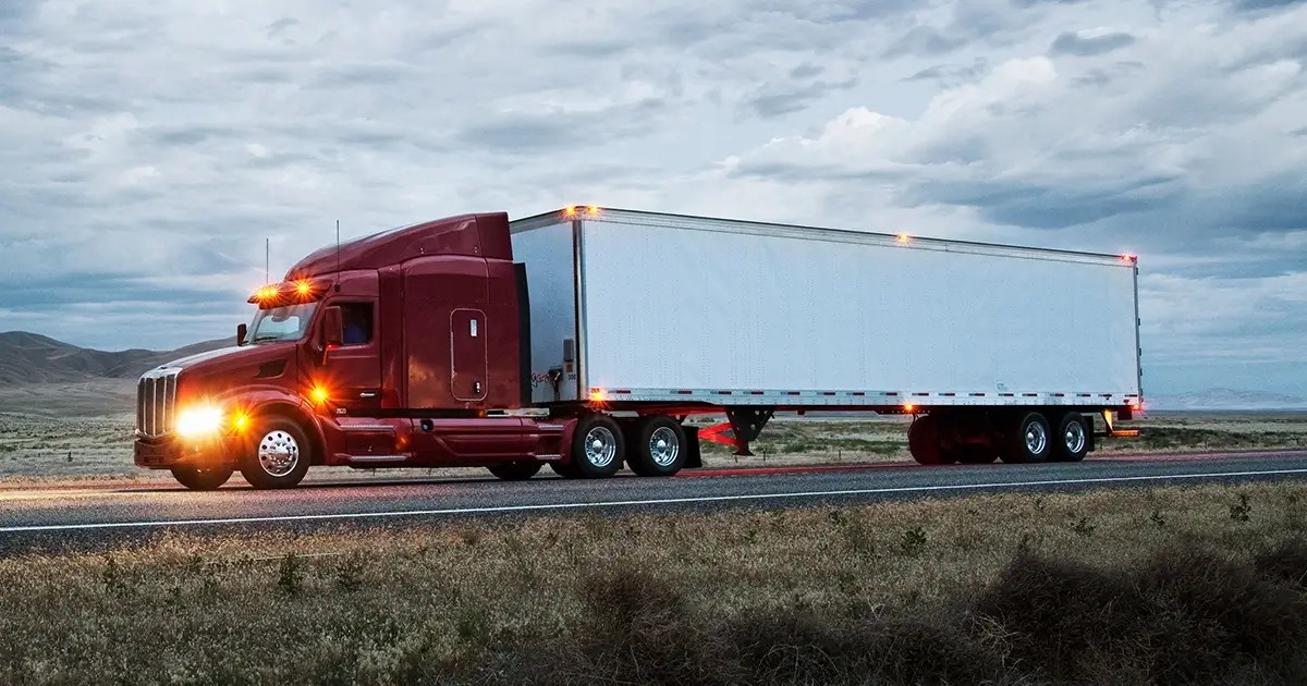 Red semi-truck with a trailer driving on a highway at dusk